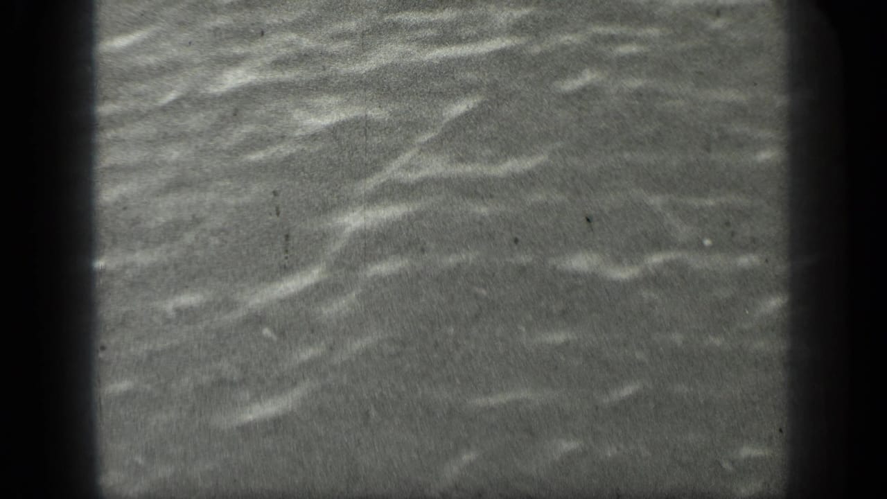 Close water surface with small bright ripples and dark vertical film edge.