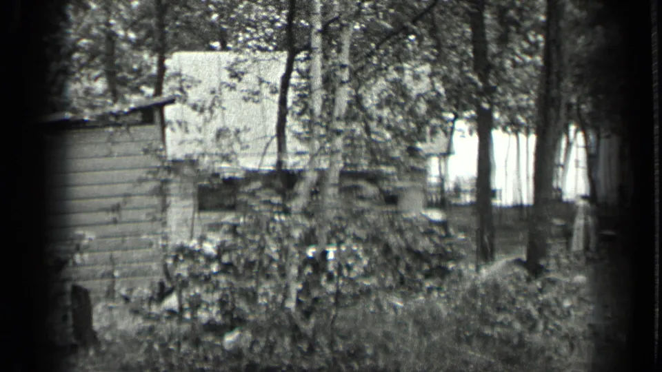 A rustic cabin or cottage appears partly obscured by trees and undergrowth in the Long Lake home-movie footage.