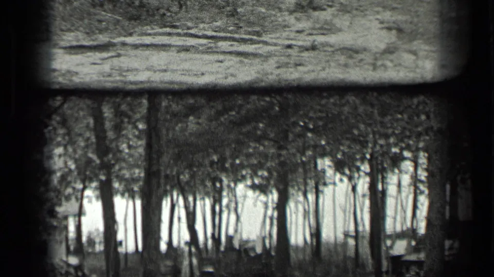 1939 Long Lake, Canada 8mm frame showing trees in front of a small shack or camp structure near a bright lakeside clearing.