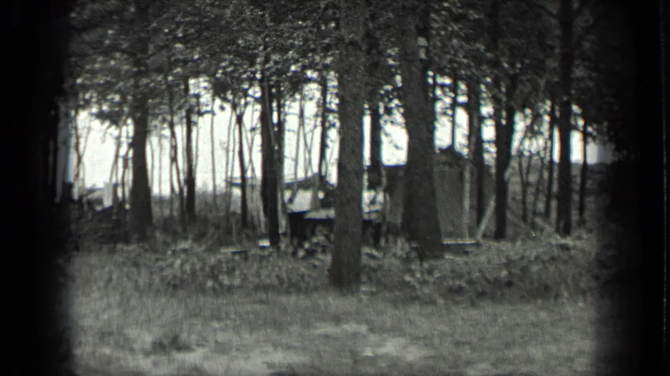 1939 home-movie frame from Long Lake, Canada, showing a shaded grove with a small building set behind the trees.