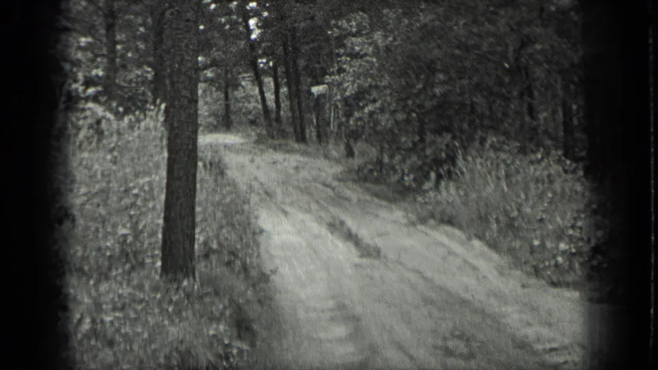 1939 Long Lake, Canada home-movie frame showing a narrow dirt road through wooded terrain with tall trees and soft film grain.
