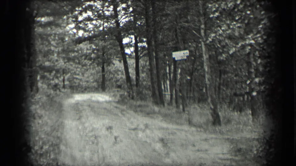 1939 Long Lake, Canada frame showing a dirt road through forest with a small sign partly visible near the trees.