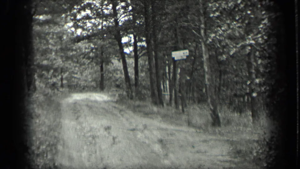 1939 Long Lake home-movie frame showing an unpaved forest path curving past trees toward a small roadside sign.