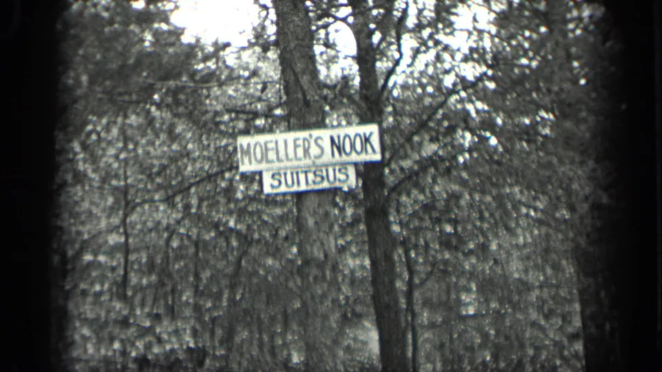 1939 Long Lake frame with a readable Moeller's Nook Suitsus sign mounted beside a tree in dense woods.