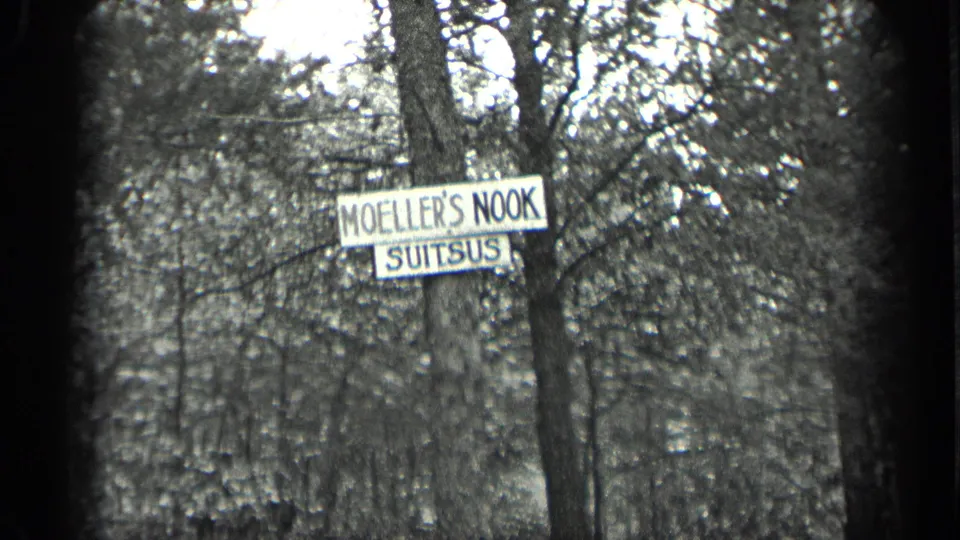 Close 1939 Long Lake view of the Moeller's Nook Suitsus sign in front of leafy woodland and a partly hidden structure.