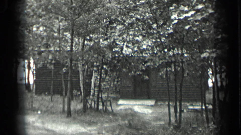 1939 Long Lake, Canada 8mm frame showing a log cabin behind slender trees, with a light bench near the front clearing.