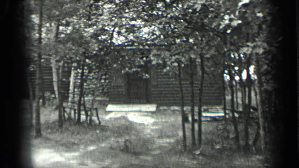 1939 Long Lake, Canada 8mm frame showing a dirt path through trees toward a rustic cabin and pale bench in a clearing.