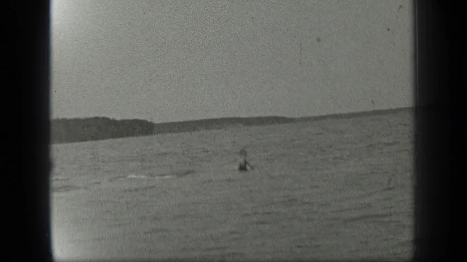 Open water at Long Lake shows a small distant swimmer below a low treeline in metadata-supported 1939 footage.