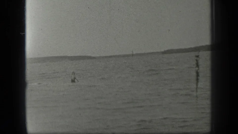 A distant swimmer sits low in the water near a vertical shoreline post on Long Lake in 1939 8mm home-movie footage.