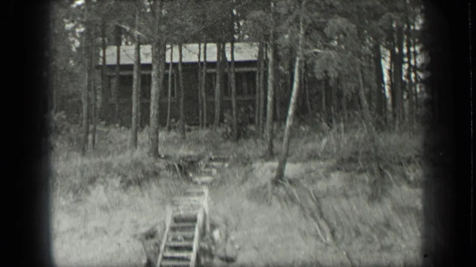 Final 1939 Long Lake frame with the stairway centered below a cabin partially obscured by slender trees and grass.