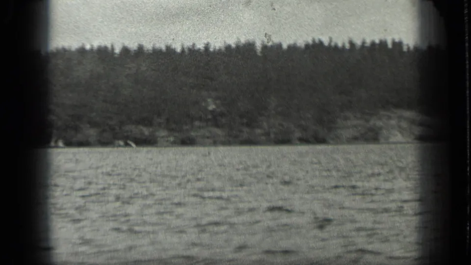 1939 Long Lake, Canada frame with rippled water in the foreground and dense forest along the far shore, seen through soft 8mm grain.