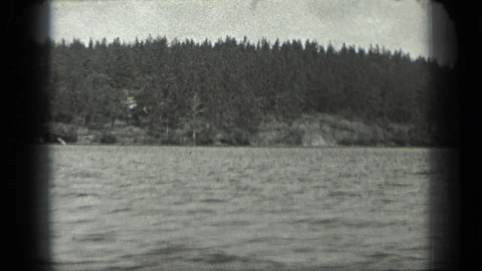 1939 Long Lake, Canada home-movie view of calm water and a tree-covered shoreline, with soft focus and rounded 8mm frame corners.