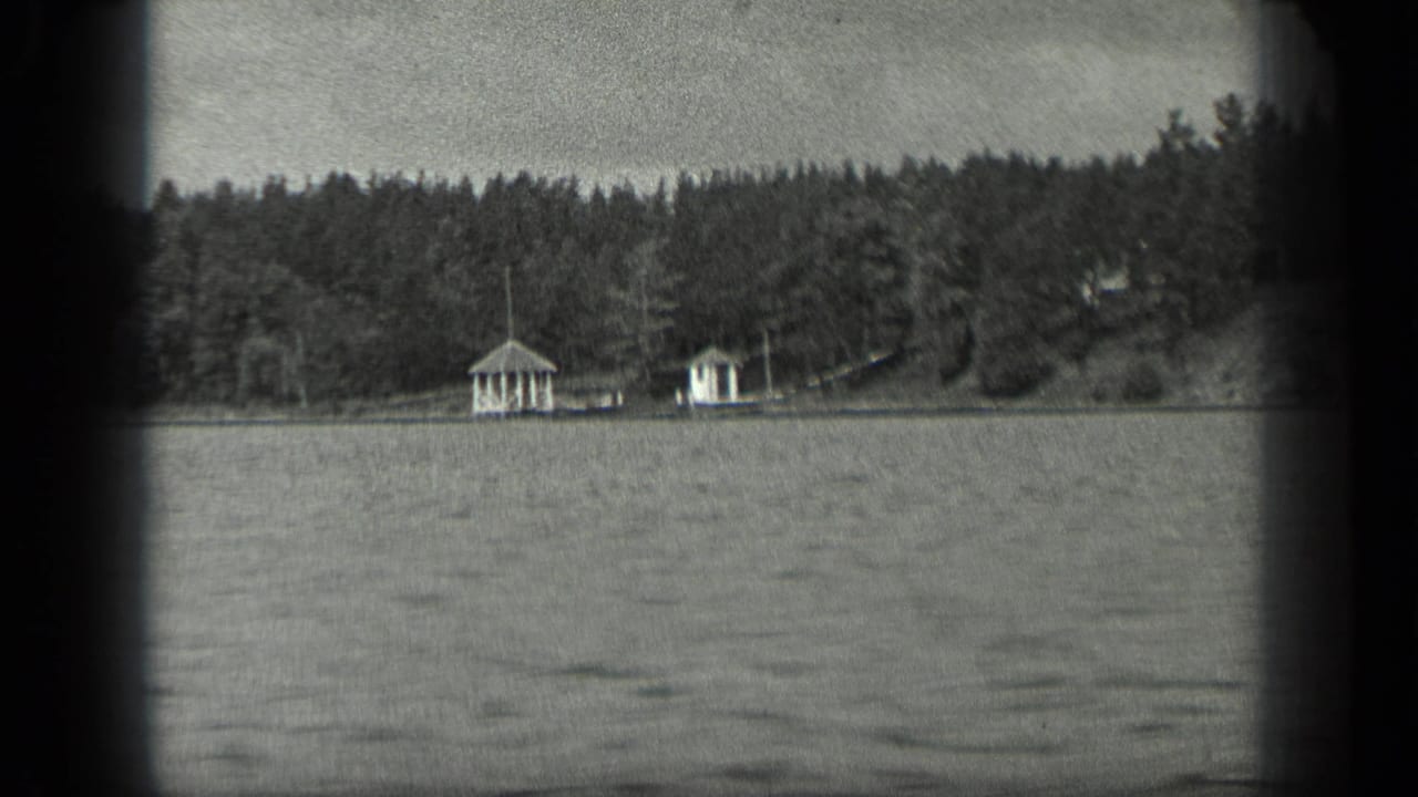 Rippling lake water facing a forested shoreline with two small white structures.