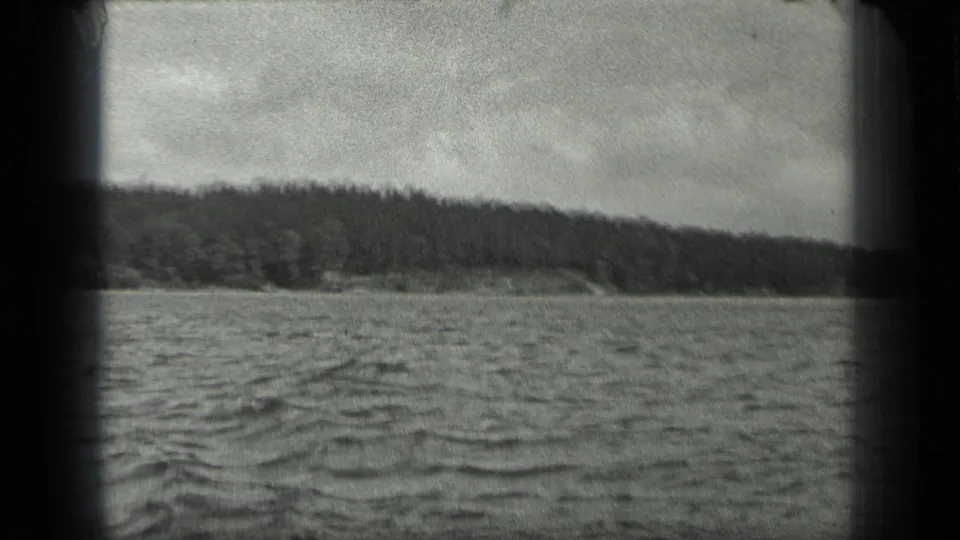 1939 8mm view from a boat on Long Lake, Canada, looking across rippled water toward a dark wooded shoreline.