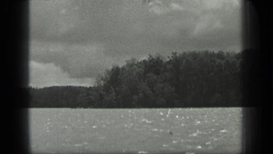 Black-and-white 1939 Long Lake footage showing rippled water and a tree-lined shore beneath clouds.