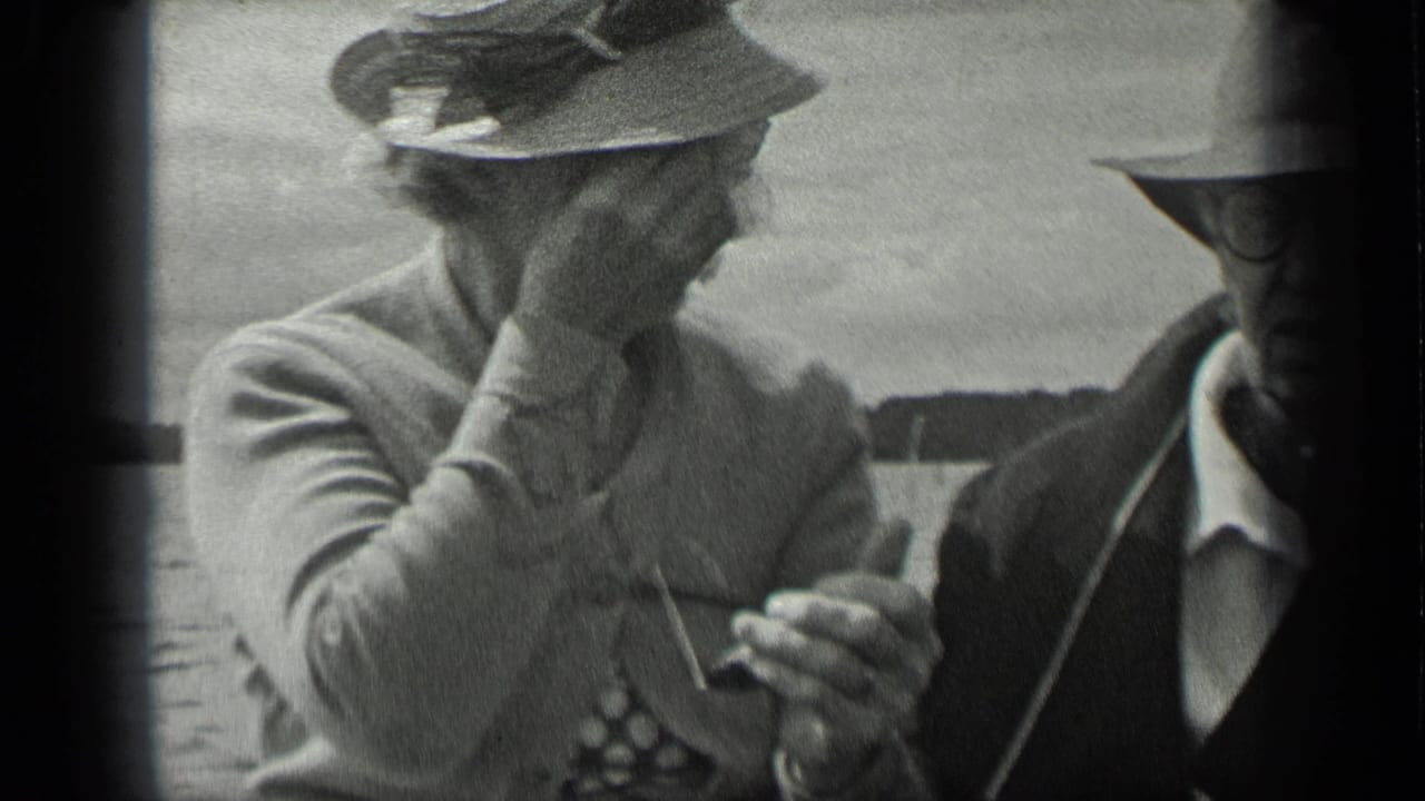 Two adults seated close together in a boat, both wearing hats and glasses near open water.