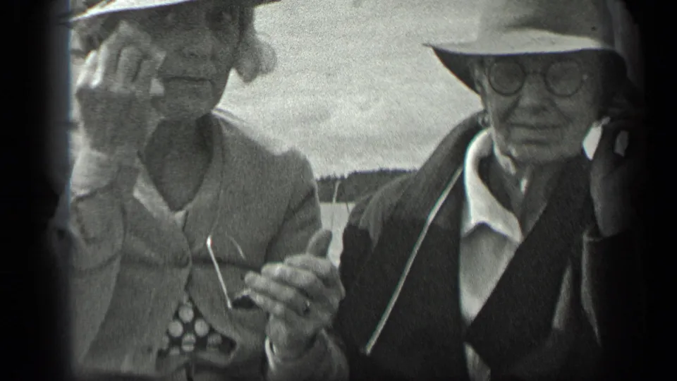 The couple remains seated on the Long Lake boat, with the woman handling her glasses and the man facing the camera in round eyeglasses.