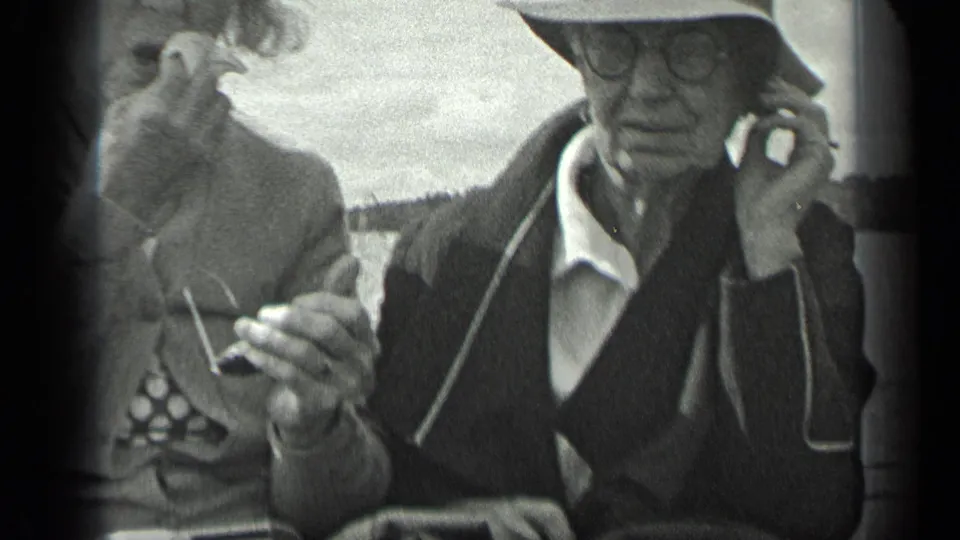 A close home-movie view shows the seated couple on the boat, the man touching his ear while the woman holds glasses in her hand.