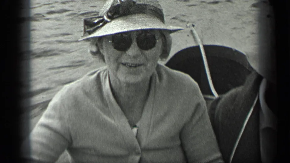 The woman smiles toward the camera in sunglasses and a wide-brimmed hat during the 1939 Long Lake boat outing.