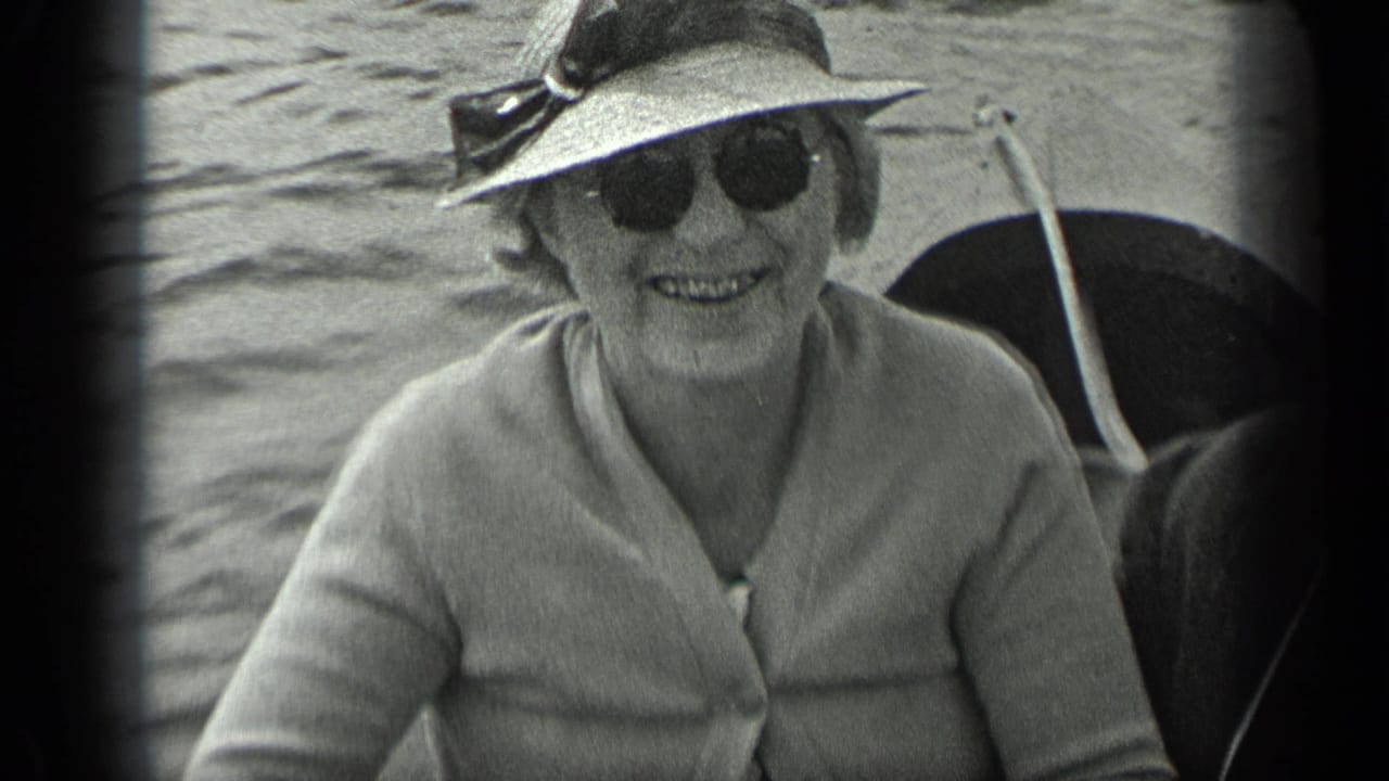 Older woman in sunglasses, hat, and light cardigan smiles from a boat on Long Lake, Canada, in 1939 home-movie footage.