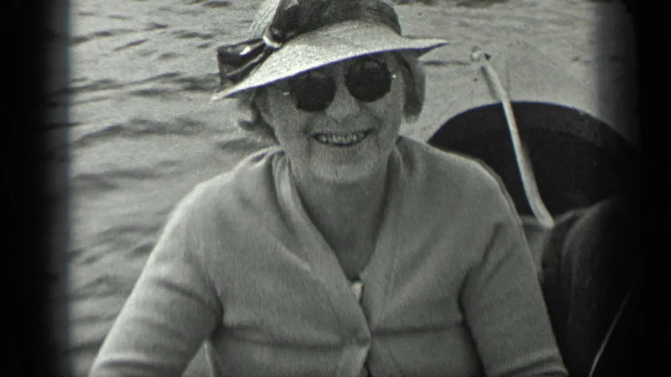 Older woman in sunglasses, hat, and light cardigan smiles from a boat on Long Lake, Canada, in 1939 home-movie footage.