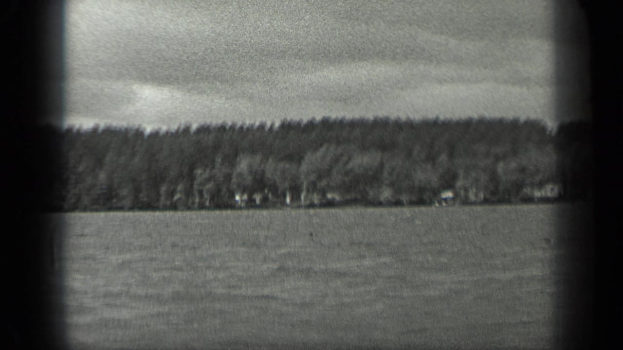 Handheld 1939 Long Lake view across rippled water toward a wooded shoreline beneath an overcast sky.