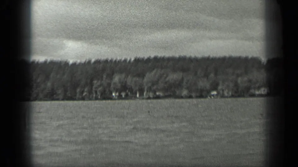 Handheld 1939 Long Lake view across rippled water toward a wooded shoreline beneath an overcast sky.