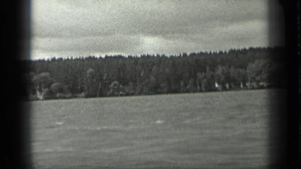 Wide black-and-white home-movie frame of Long Lake, Canada, showing water, forested shore, and cloudy sky in 1939.