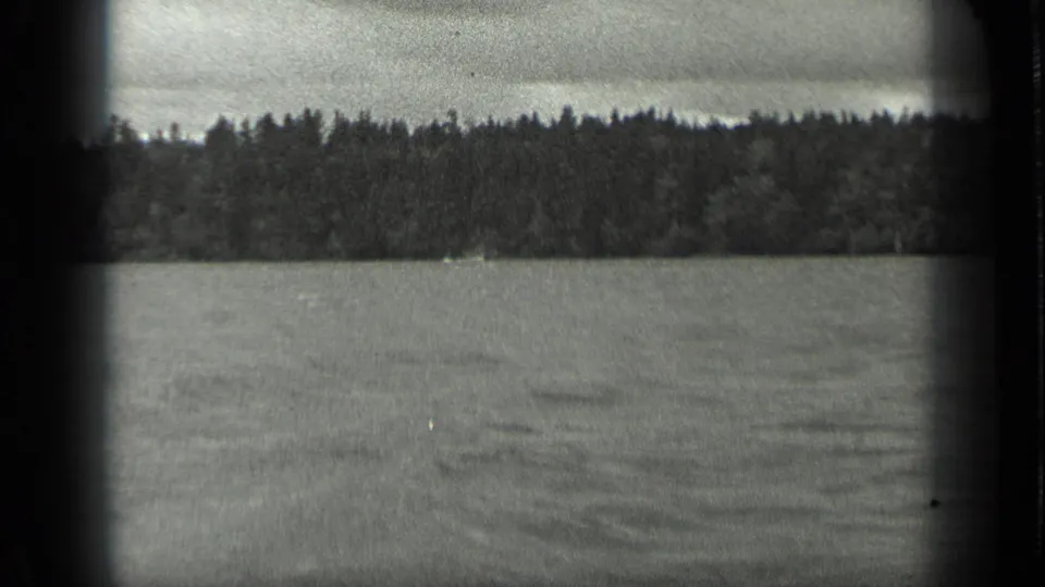1939 home-movie frame from Long Lake, Canada, with rippled water in front and a dark band of trees along the far shore.