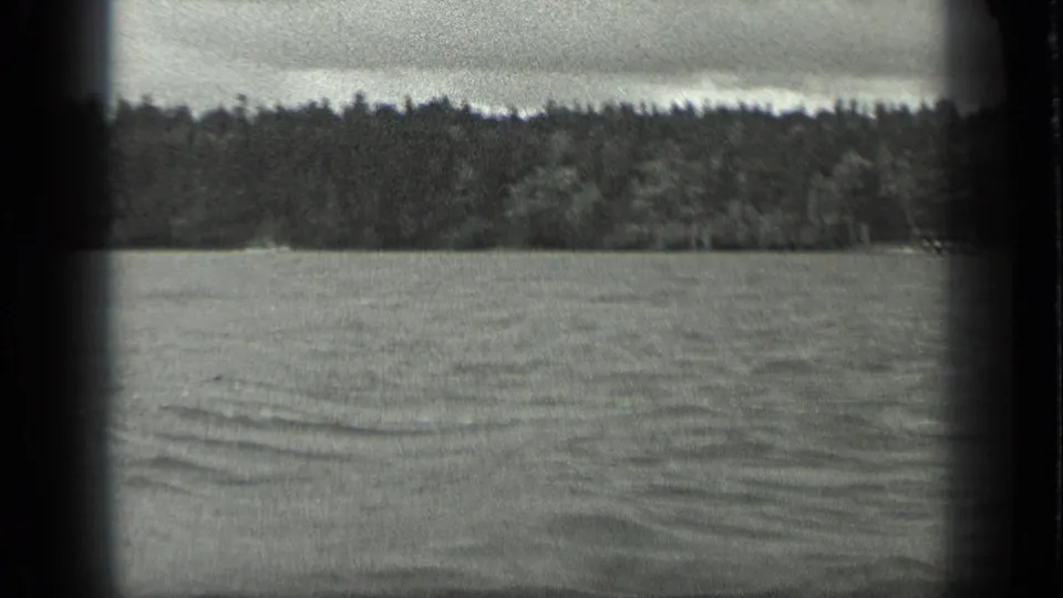 Long Lake, Canada, in 1939, seen from a boat with rippled water, wooded shore, cloudy sky, and a small indistinct light shape near shore.