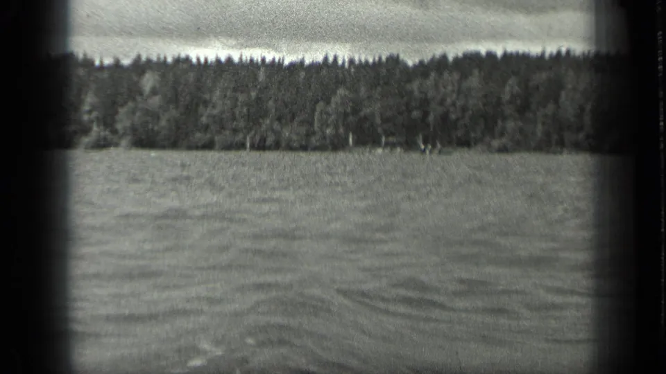 Black-and-white 8mm frame of Long Lake, Canada, showing rippled water and a dense wooded shore in the distance.