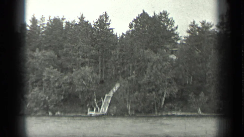 Long Lake shoreline in 1939 home-movie footage, with trees and a small wooden dock or stair structure at the water's edge.