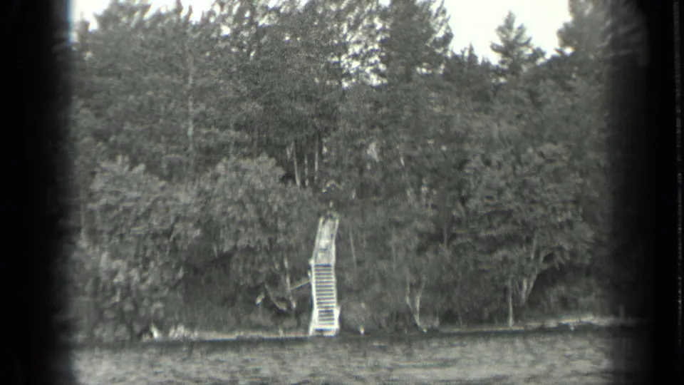 1939 Long Lake, Canada home-movie frame showing rippled water, dense trees, and a pale dock structure along the shoreline.