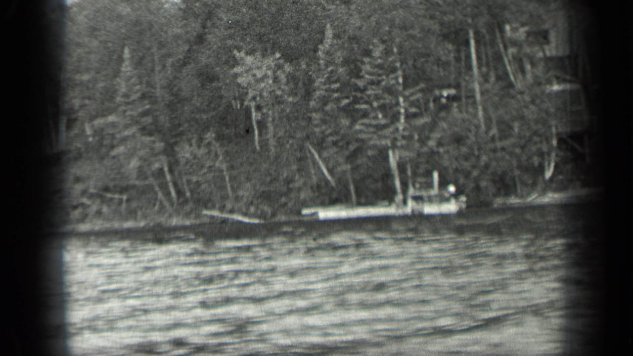 Small boat on calm lake near a wooded shoreline, seen through dark 8mm frame edges.