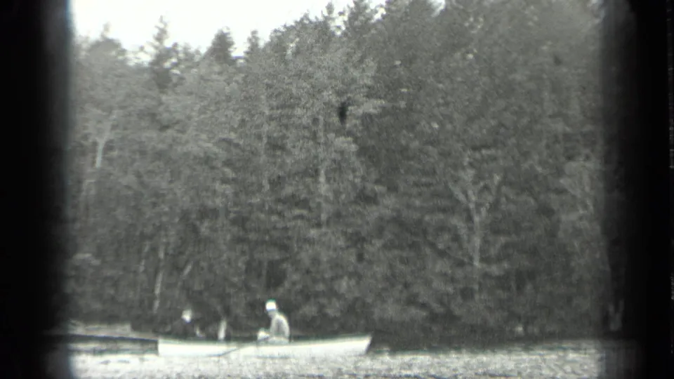 1939 Long Lake, Canada home-movie frame showing a man seated in a small rowboat near the wooded lakeshore.