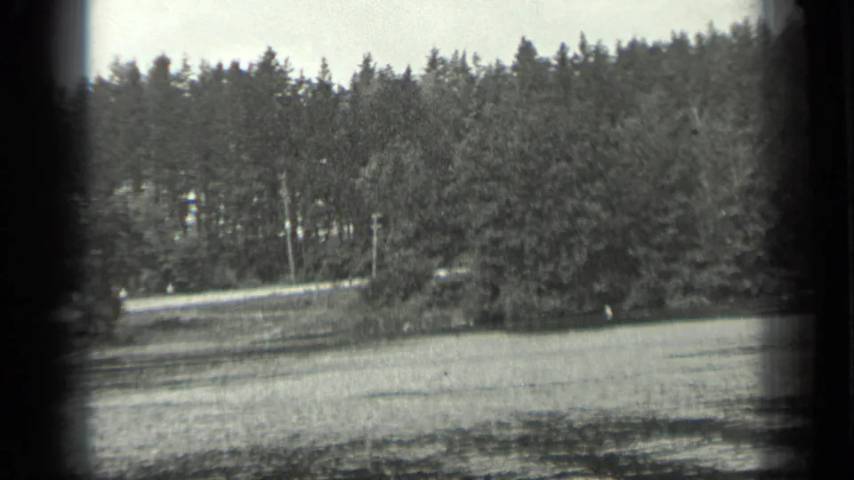Black-and-white Canadian lake frame with rippling water, dense trees, and visible 8mm frame-edge shadows.