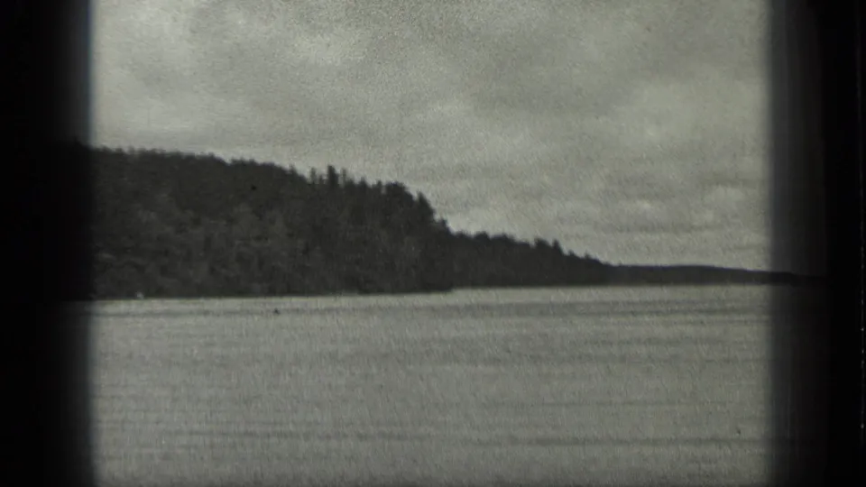 1939 Long Lake, Canada home-movie frame with a dark wooded point, broad water surface, distant shore, and cloudy sky.