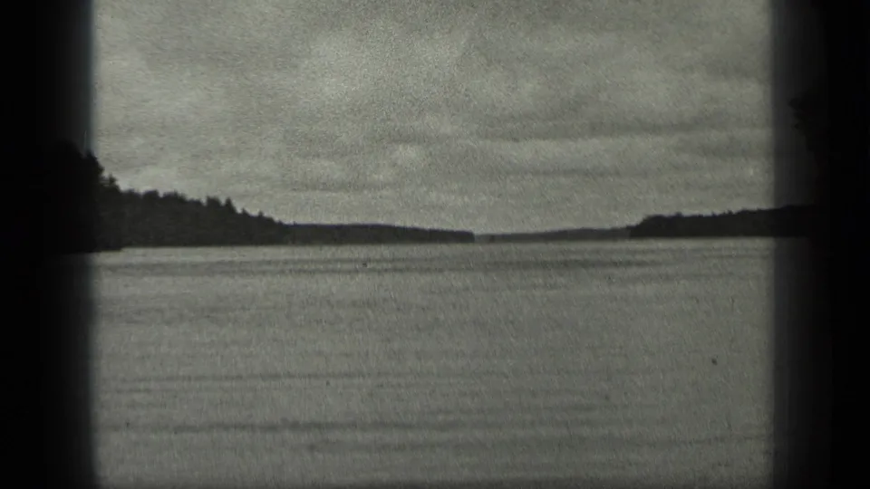 1939 Long Lake, Canada home-movie frame showing calm water, distant tree-lined shore, and cloudy sky in black-and-white 8mm.