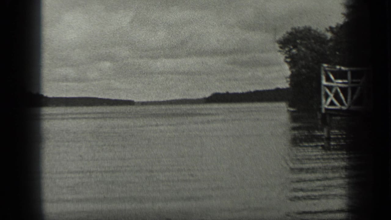 1939 Long Lake, Canada frame with calm water, distant shoreline, trees, and a white wooden dock or platform along the right edge.