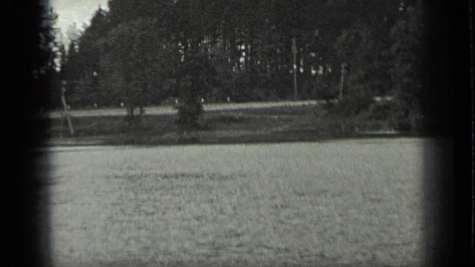 1939 Long Lake, Canada frame showing calm water in the foreground and a wooded lakeshore with a small open strip near the bank.