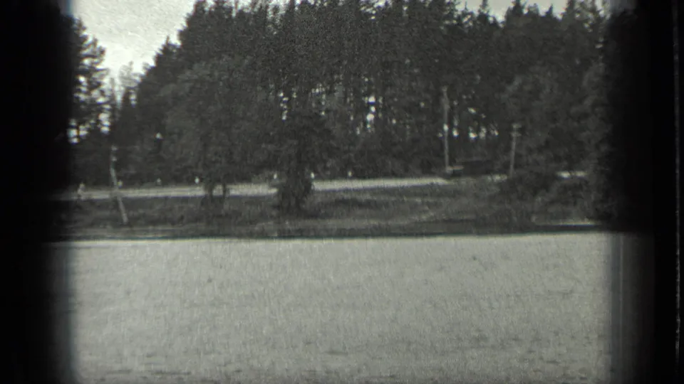 A grainy 8mm view of Long Lake, Canada, with water in the foreground and dense trees along the far bank.