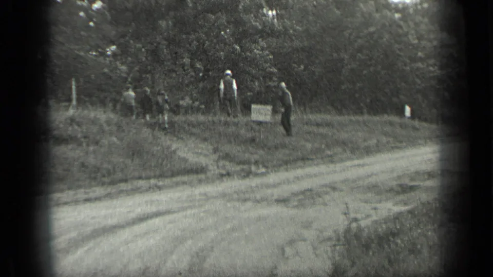 At Long Lake in 1939, several distant men stand beside a dirt road near trees and a small roadside marker.