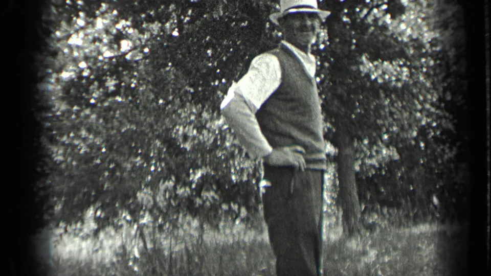 A man in period clothing poses with one hand on his hip outdoors in Long Lake, Canada, surrounded by trees in 1939 footage.