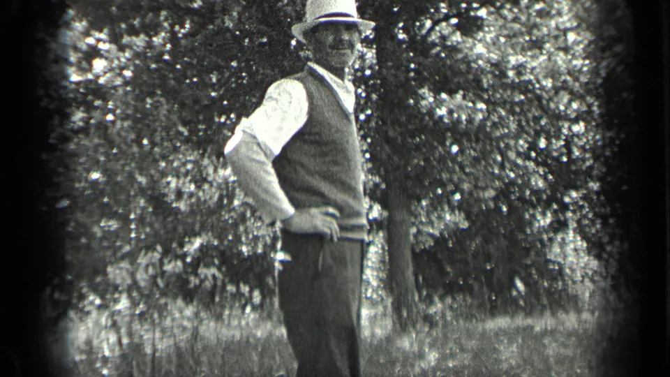 1939 Long Lake, Canada frame of a man in a brimmed hat and vest standing outdoors beside leafy trees.