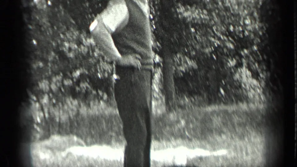 1939 Long Lake home-movie frame showing an adult man standing in a grassy outdoor area, partly cropped by the camera.