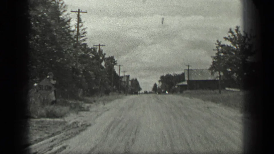 Long Lake, Canada road view with a partially visible roadside sign at left, utility poles, trees, and a low building beyond the road.