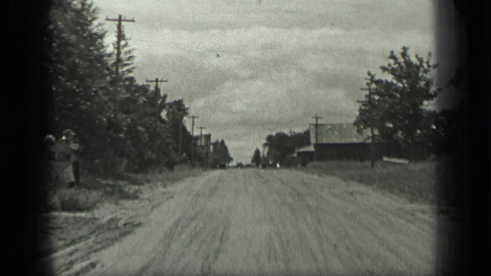 A 1939 rural Long Lake road scene with trees, utility poles, buildings, and a woman beginning to appear along the left roadside.
