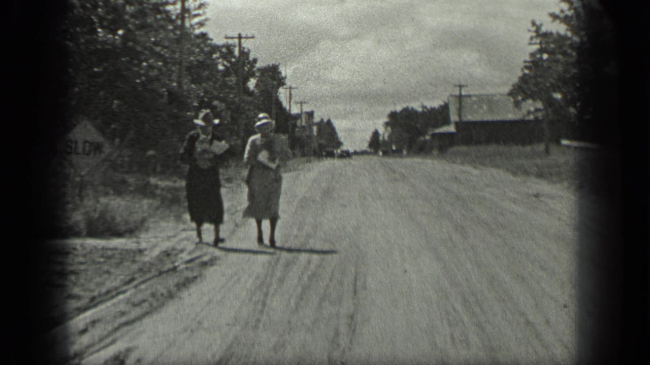 Two women continue walking on the road beside trees and utility poles.