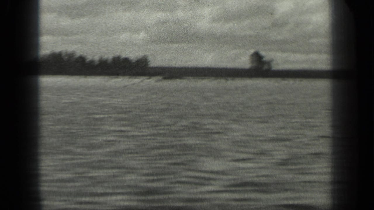 1939 8mm home-movie frame of Long Lake, Canada, showing rippled water, low tree line, and cloudy sky through dark film-frame edges.