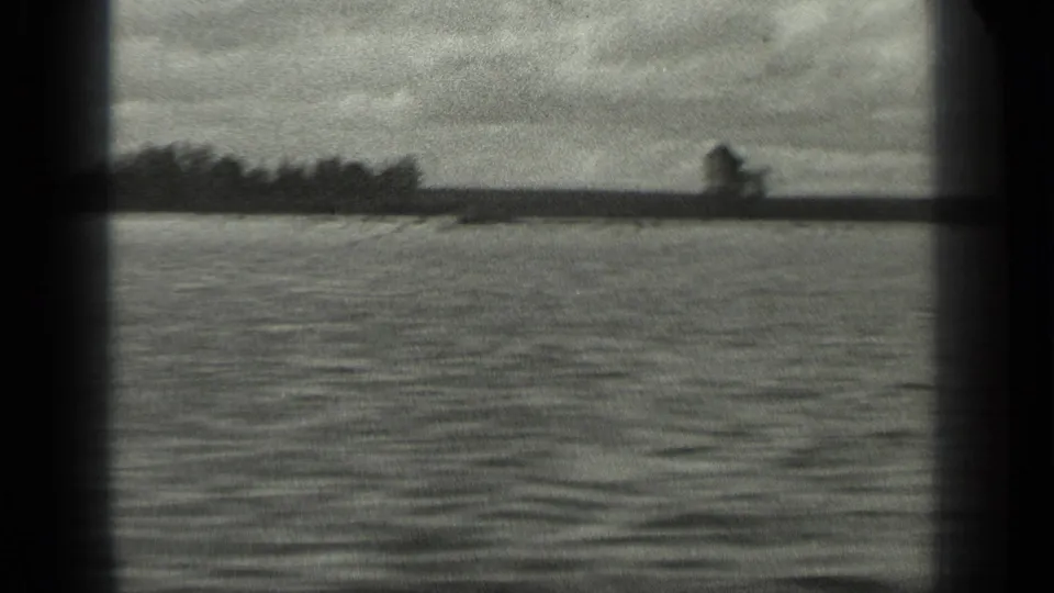 1939 8mm home-movie frame of Long Lake, Canada, showing rippled water, low tree line, and cloudy sky through dark film-frame edges.